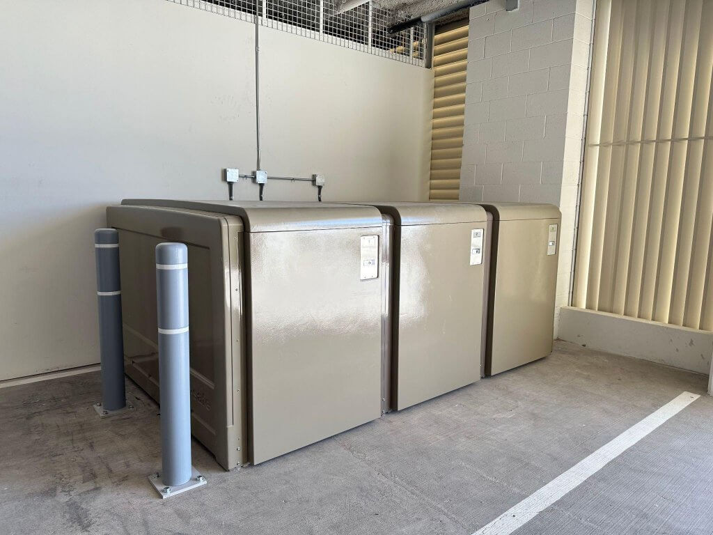 Row of CycleSafe bike lockers inside a covered shelter on a college campus.